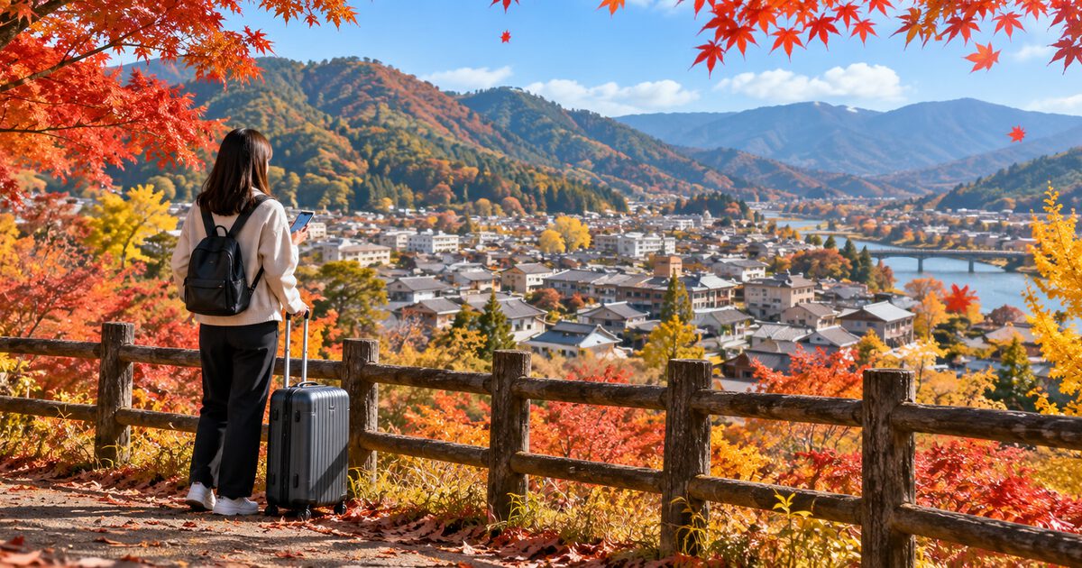 A traveler with a suitcase at a hillside lookout above a small town in autumn colors